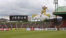 Black billboard next to stadium, with "JESUS" in white letters