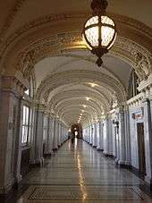 A long hallway with marble walls and columns, vaulted ceilings, and a person walking near the far end.