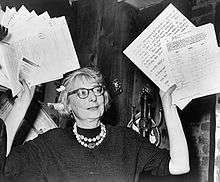 Woman in glasses waving documents in air.