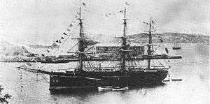 Three-masted warship at anchor in a bay.
