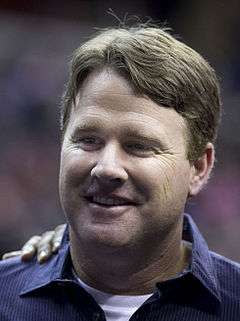 Color head-and-shoulders photograph of smiling white man (Jay Gruden), wearing dark blue sport shirt.
