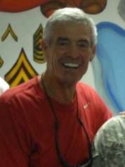 Cropped photograph of Mora in a red t-shirt posing with members of the U.S. military