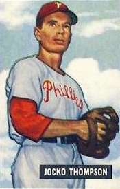 A middle-aged man in a white pinstriped baseball uniform looks into the camera while facing to the left side. He is wearing a baseball cap with a white "P" on the front, and his jersey reads "Phillies" across the chest.
