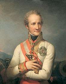 Painting of a curly-haired man with his arms folded across his chest. He wears an elaborate white military coat with gold braid and a large decoration.