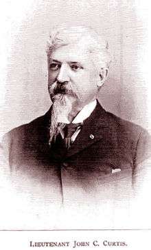 Head and shoulders of an older white man with Van Dyke mustache and goatee wearing a dark suit over a white shirt and dark tie. Below are the words "LIEUTENANT JOHN C. CURTIS".