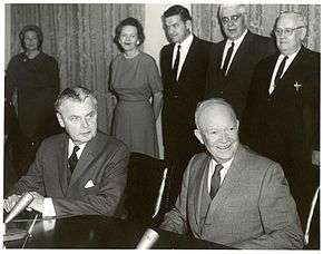 Diefenbaker and a Dwight Eisenhower sit at a table. Two women and three men stand behind them.