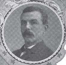 Portrait of a man with a drooping mustache and a dark suit coat, in a circular frame.