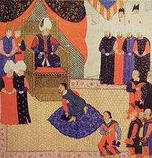A bearded young man on his knees before a bearded old man who wears a turban and sits on a throne in a tent