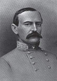 A man with receding dark hair and a full, dark mustache wearing a high-collared military jacket