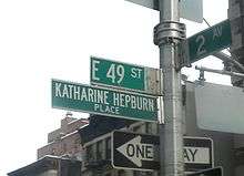 A street sign that reads "E 49 St", with another underneath it that reads "Katharine Hepburn Place".