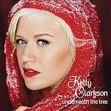 A blonde woman whose head is wrapped in a red scarf and covered with snow, on the lower right, the wordmarks "Kelly Clarkson" and "Underneath the Tree" are printed in stylized "Feel Script" and "Bree" typefaces.