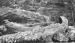 A black and white photo of a partially ruined wall from above.
