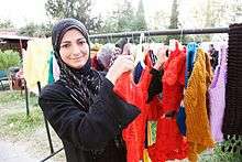 A Syrian refugee stands next to the clothes she has knitted for sale.
