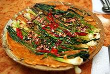 A plate of a colorful pancake made with green scallions, sliced red chili pepper and chopped seafood