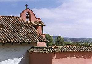 Photograph of the campanile of La Purisima Mission, flanked by low stucco buildings with tile roofs.