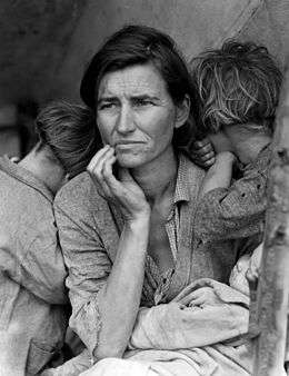 A haggard middle-aged woman in looks plaintively into the distance. Two children bury their faces into her shoulders. The woman and children are both dressed in shabby, drab clothing.