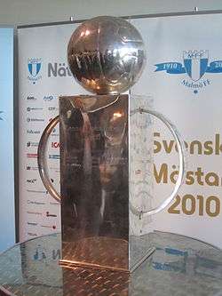An impressive trophy of a somewhat cubist fashion. Made of silver, it comprises a large socle, a large semi-circular handle on each side and a depiction of an old-fashioned leather football on top. The words "Lennart Johanssons Pokal" can be seen engraved on the front.