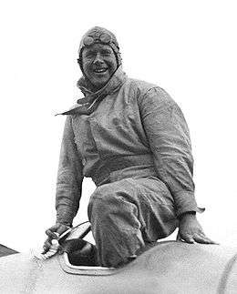 Informal half portrait of man in flying suit with cap and googles emerging from the open cockpit of an aeroplane