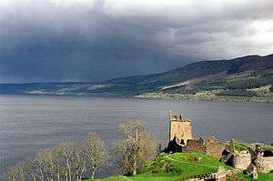 The loch on a cloudy day, with ruins of a castle in the foreground