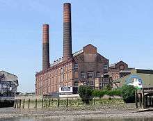 A large red-brick building with a double-pitched roof stretches into the distance. Two cylindrical chimneys reach high into the sky.