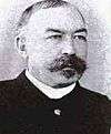 A black and white photo of Louis Carpenter, a white male. He has a mustache and Goutea, his hair is colmbed back and he is wearing a jacket and white shirt