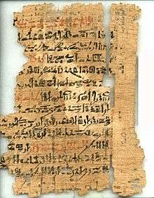 An ancient, torn and fragmented papyrus document, with cursive hieratic handwriting in black and red ink on its surface