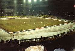 Football match with snow covering the stadium lanes and spectators wearing winter gear