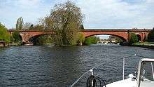 a red brick built bridge with shallow arches spanning a river, viewed from the front of a small boat