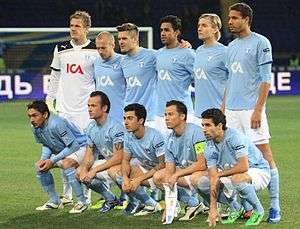 An association football team. A team of players in light blue shirts, white shorts and light blue socks, poses on a pitch for a formative shot.
