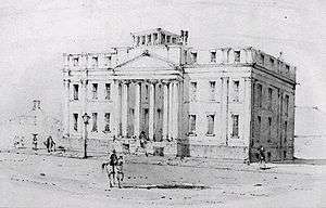 Black and white drawing of a large three-storey building fronted by a four-column portico. A man on a light-coloured horse is riding down the wide empty street in front of the building.