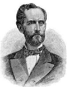 Head and shoulders of a white man with a full beard wearing a suit coat and bow tie.