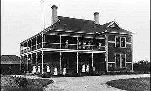 A large Federation style brick building with verandas and balconies, on which a dozen women in white are standing.