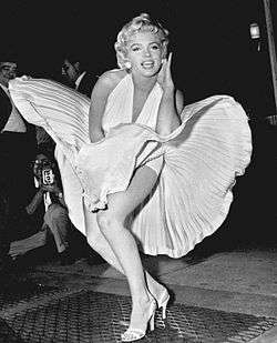Monroe is posing for photographers, wearing a white halterneck dress, which hem is blown up by air from a subway grate on which she is standing.