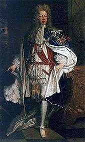 A man in robes of the Order of the Garter. The man is wearing white and red clothing, with a mantle adorned with a large badge.