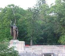 Large bronze statue of man carrying a cross, surrounded by trees.