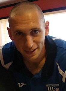 A young man with a shaven head, wearing a blue and white T-shirt