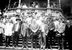 A crown of approximately 40 men standing on a set of steps in front of stone balcony
