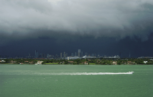 Black rain clouds darken the sky over tropical waters with the city of Miami in the background.