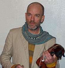 Michael Stipe looking to the left of the camera, holding a bag and digital media player