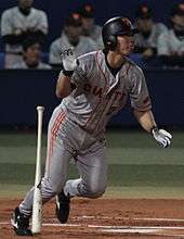 Michihiro Ogasawara wearing a gray baseball uniform and black baseball helmet running and dropping a baseball bat