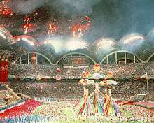 Crowds of people are gathered in a stadium with fireworks.