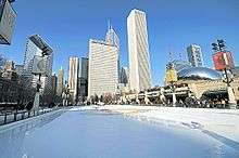 An empty ice skating rink with tall buildings in the background