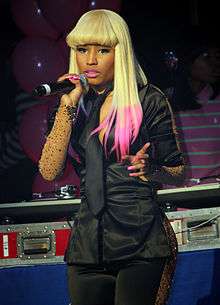A portrait of Nicki Minaj in a black outfit singing into a microphone.
