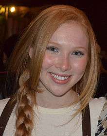 An eighteen-year-old redheaded female is wearing a beige shirt with her ponytail draped over her right shoulder; she is smiling into the camera.