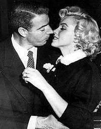 Close-up of Monroe and DiMaggio kissing; she is wearing a dark suit with a white fur-collar and he a dark suit
