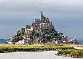 The buildings of Mont Saint Michel sit on a rocky island that rises above the surrounding fields and bay