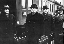 A group of four men wearing hats and a train behind.