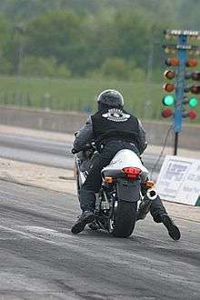 A rider in black jeans and tennis shoes seen from behind on a Suzuki Hayabusa motorcycle, with a green light to his right.