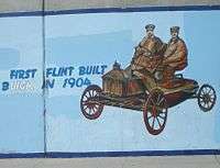Mural of old car with two passengers against light-blue background