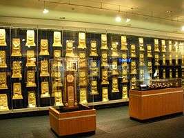 A room with glass display cases containing rectangular, wooden trophies that are gold-plated.